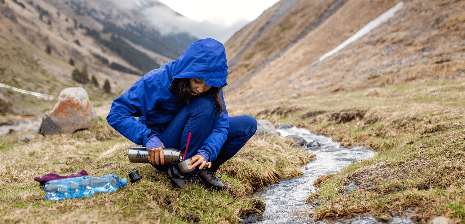 woman in camping gear pouring water into thermos